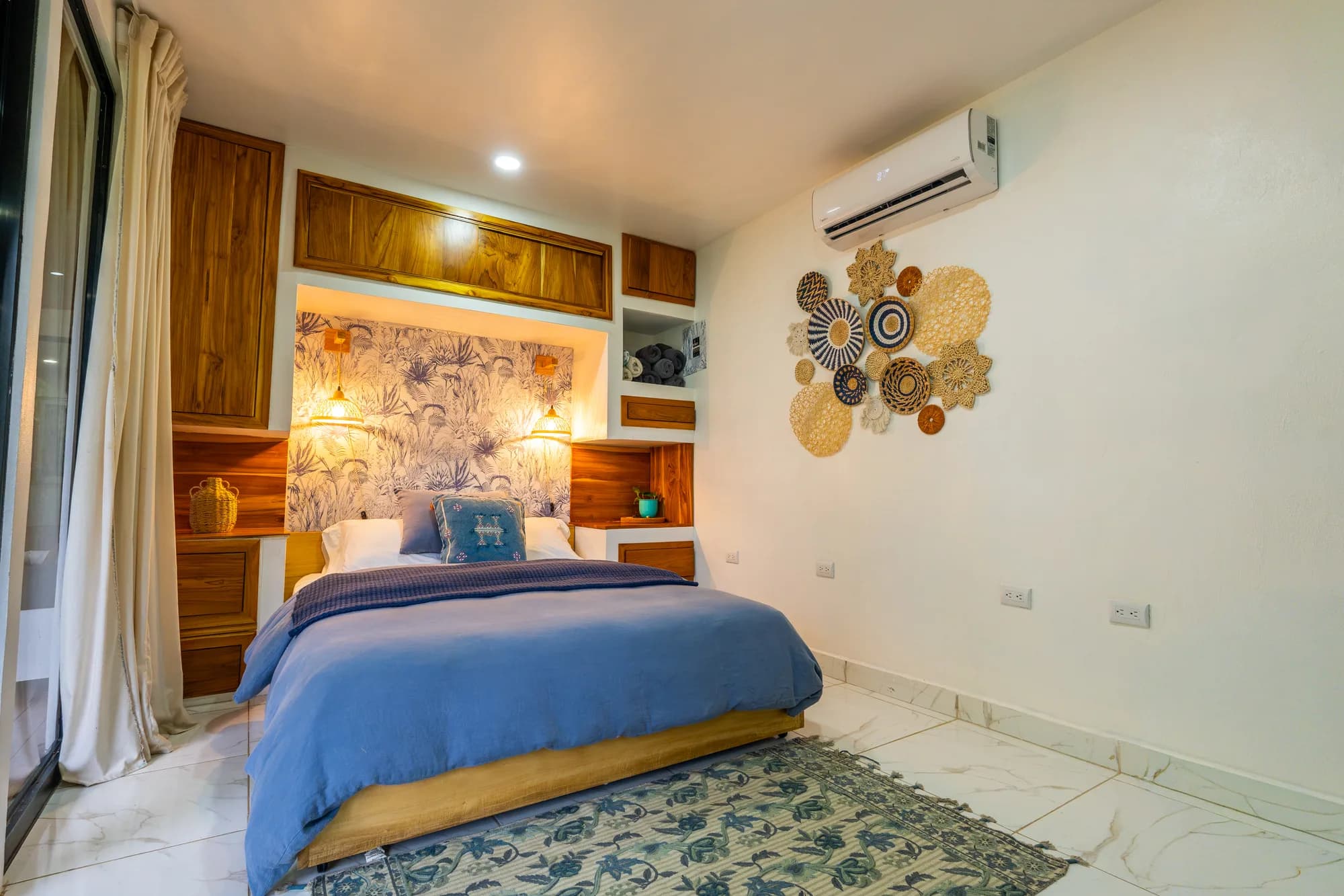 Morpho House bedroom with custom wood built-in bed nook, blue bedding, and woven pendant lights