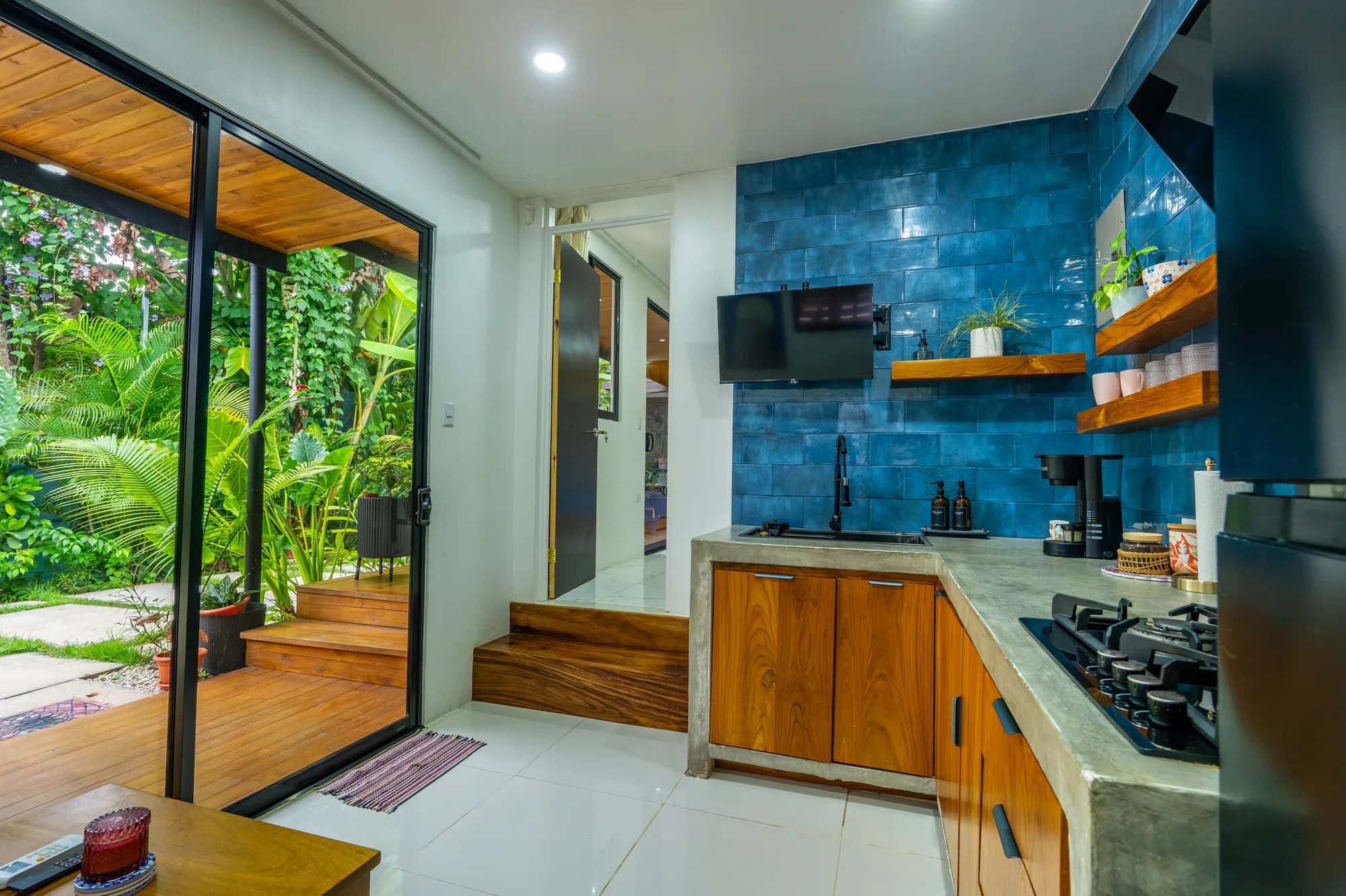 Morpho House kitchen with blue tile backsplash and open door to a tropical garden deck